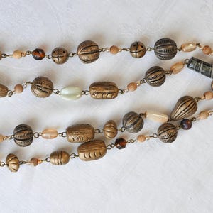 May include: A long necklace made of brown and gold beads with a variety of shapes and sizes. The necklace is strung on a silver chain and has a variety of beads, including round, oval, and rectangular beads.