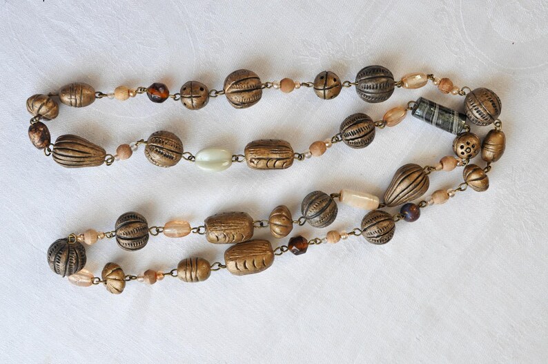 May include: A long necklace made of brown and gold beads with a variety of shapes and sizes. The necklace is strung on a silver chain and has a variety of beads, including round, oval, and rectangular beads.