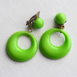 Könnte beinhalten: Ein Paar limegrüne Ohrclips mit einem Kreisdesign. Die Ohrringe haben eine kleine grüne Kugel oben.