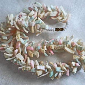 Peut inclure: Un long collier composé de petites pièces irrégulières de coquillages blancs, roses et bleus. Le collier est enfilé sur un cordon blanc avec un fermoir doré.