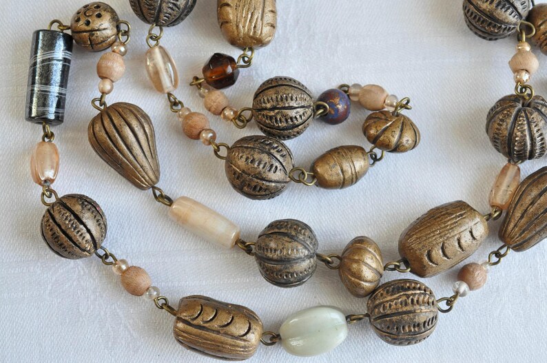 May include: A long, multi-strand necklace with brown, beige, and white beads. The beads are made of various materials, including metal, wood, and glass. The necklace is strung on a silver chain.