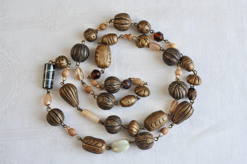 May include: A long necklace made of brown and gold beads. The beads are various shapes and sizes, including round, oval, and rectangular. Some of the beads have intricate designs.