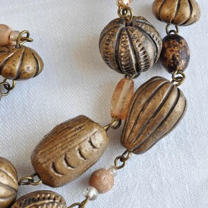 May include: A necklace made of brown and gold beads with a variety of textures and shapes. The beads are strung on a silver chain.