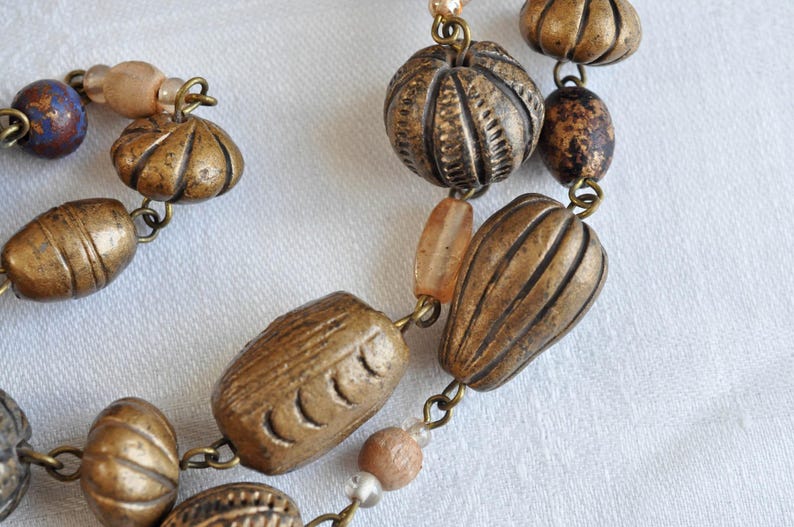 May include: A necklace made of brown and gold beads with a variety of textures and shapes. The beads are strung on a silver chain.