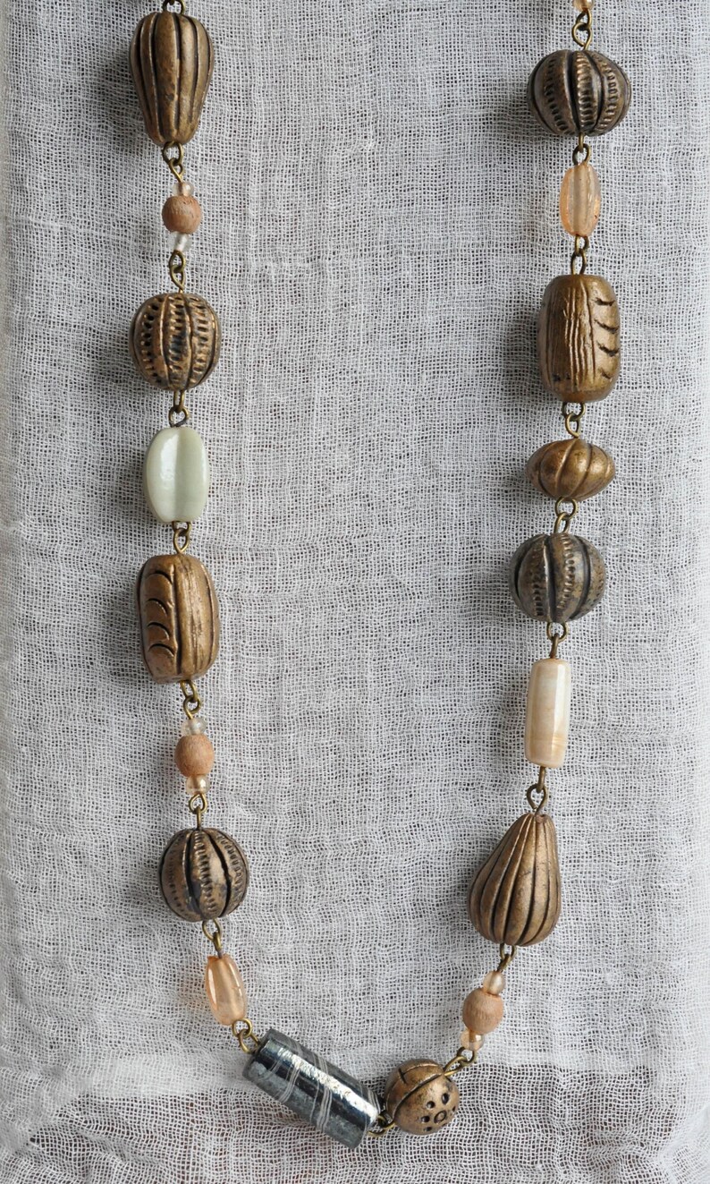 May include: A necklace with brown and beige beads, including a long, cylindrical bead with a gray and white pattern.