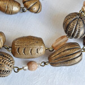 May include: A necklace made of brown and gold beads. The beads are various shapes and sizes, including round, oval, and rectangular. The necklace is strung on a silver chain.