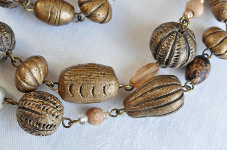 May include: A necklace made of brown and gold beads. The beads are various shapes and sizes, including round, oval, and rectangular. The necklace is strung on a silver chain.