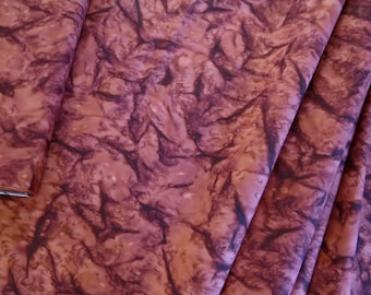 May include: A close-up of a fabric with a brown and purple marbled pattern. The fabric is folded and has a soft, smooth texture.