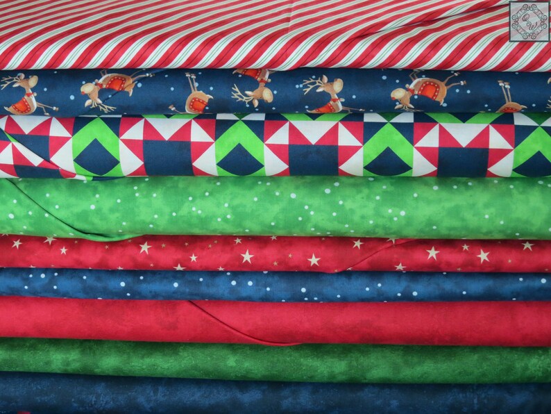 May include: A stack of eight different fabric prints in a variety of Christmas themes. The fabrics include red and white stripes, blue with reindeer, green with white dots, red with white stars, blue with white dots, red, green, and blue.
