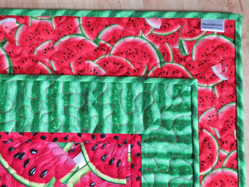 Puede incluir: Una tela acolchada verde y roja con un patr&oacute;n de sand&iacute;a. La tela tiene un borde verde y una etiqueta que dice "QuiltsbyJeni QuiltsbyJeni.com".