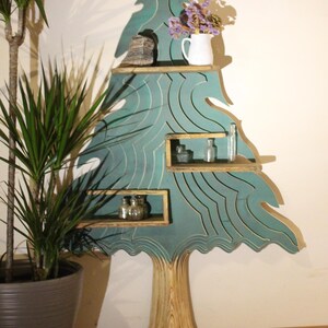 May include: A teal blue wooden tree-shaped shelf with four shelves. The shelves are decorated with a wavy pattern. The tree has a natural wood trunk. The shelf is decorated with a vase of purple flowers, a small rock, and glass bottles.