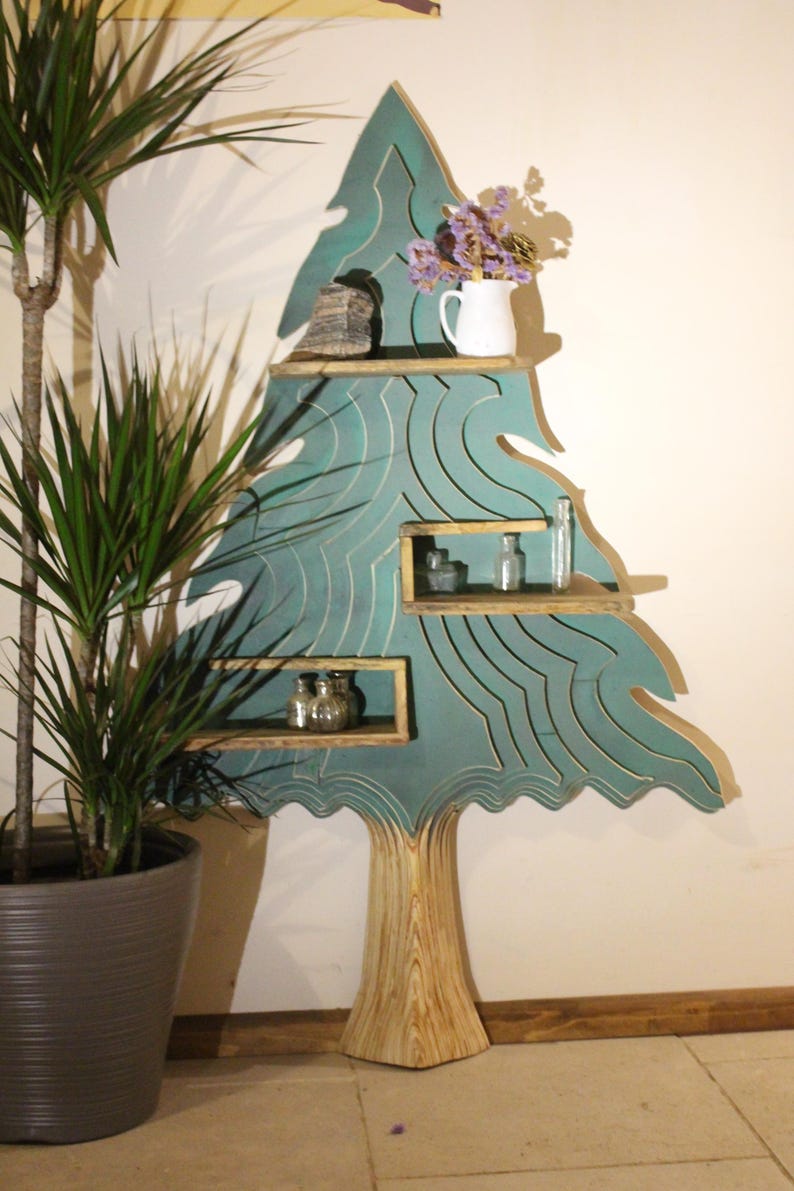 May include: A teal blue wooden tree-shaped shelf with four shelves. The shelves are decorated with a wavy pattern. The tree has a natural wood trunk. The shelf is decorated with a vase of purple flowers, a small rock, and glass bottles.
