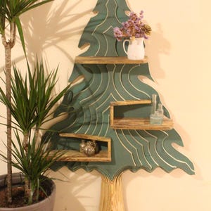 May include: A teal green wooden tree-shaped shelf with three shelves. The shelves are made of natural wood and the tree trunk is made of a light wood. The shelf is decorated with a white vase with dried flowers and small glass bottles.