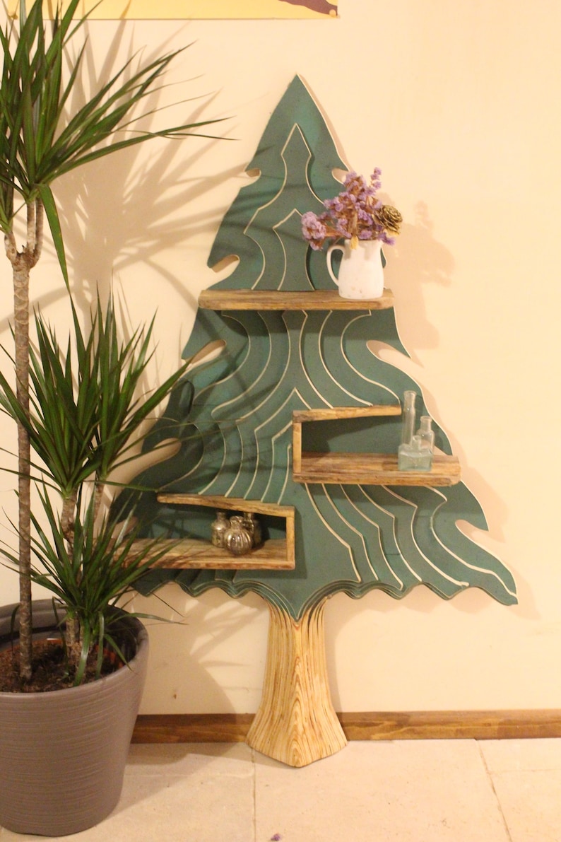 May include: A teal green wooden tree-shaped shelf with three shelves. The shelves are made of natural wood and the tree trunk is made of a light wood. The shelf is decorated with a white vase with dried flowers and small glass bottles.