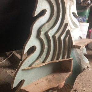 May include: A wooden shelf unit with a unique wave-like design. The shelves are made of plywood and have a light blue paint finish. The unit has multiple shelves of varying sizes and shapes.
