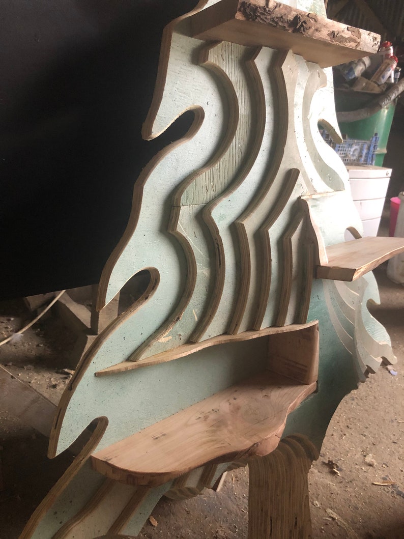 May include: A wooden shelf unit with a unique wave-like design. The shelves are made of plywood and have a light blue paint finish. The unit has multiple shelves of varying sizes and shapes.