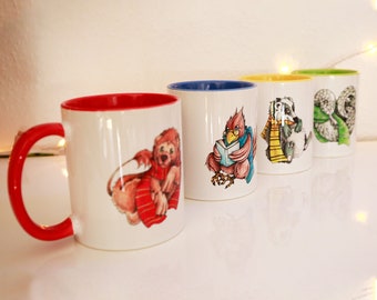Puede incluir: Cuatro tazas de cerámica con bordes rojos, azules, amarillos y verdes. Cada taza presenta un personaje animal ilustrado diferente. La primera taza tiene un borde rojo y presenta un león rojo y marrón con una bufanda. La segunda taza tiene un borde azul y presenta un pájaro rojo con una bufanda azul leyendo un libro. La tercera taza tiene un borde amarillo y presenta un tejón negro y blanco con una bufanda amarilla. La cuarta taza tiene un borde verde y presenta un búho verde y blanco con una bufanda verde.