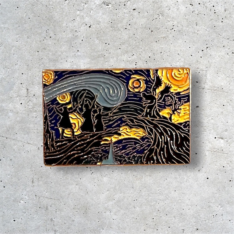 K&ouml;nnte beinhalten: Eine goldfarbene Emaille-Anstecknadel mit einer Nachbildung von Vincent van Goghs Gem&auml;lde "Sternennacht". Die Anstecknadel zeigt einen wirbelnden Nachthimmel mit einem leuchtend gelben Mond und Sternen, einem dunklen Zypressenbaum und drei Figuren im Vordergrund.
