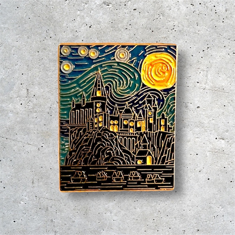 K&ouml;nnte beinhalten: Eine goldfarbene Emaille-Anstecknadel mit einer Schwarzwei&szlig;-Illustration von Hogwarts Castle im Stil von Vincent van Goghs Sternennacht. Die Anstecknadel hat einen blauen, gr&uuml;nen und gelben Hintergrund mit einem gelben Mond.