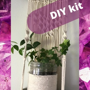 May include: A macrame plant hanger DIY kit with a glass jar planter holding green plants. The macrame is off-white and hangs from a wooden dowel. The text "DIY kit" is overlaid on the image.