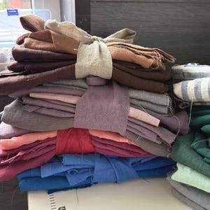 Peut inclure: Une pile de lots de tissus pliés dans diverses couleurs, notamment marron, beige, mauve, rose, rouge et bleu, maintenus par des bandes de tissu. Une surface blanche avec une règle imprimée indiquant 40 cm est visible sous les tissus.