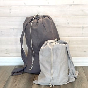 Peut inclure: Deux sacs en lin à cordon de serrage, un gris foncé et un gris clair, sont présentés côte à côte. Les sacs ont de longues sangles en tissu et des cordons blancs. Les sacs sont en tissu doux et texturé, pour le rangement ou le linge.