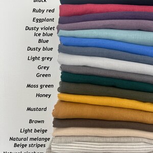 May include: A stack of folded fabric samples in various colors, including white, black, ruby red, and mustard. The image displays the names of the colors: White, Black, Ruby red, Eggplant, Dusty violet, Ice blue, Blue, Dusty blue, Light grey, Grey, Green, Moss green, Honey, Mustard, Brown, Light beige, Natural melange, Beige stripes, Natural gingham, and Natural.