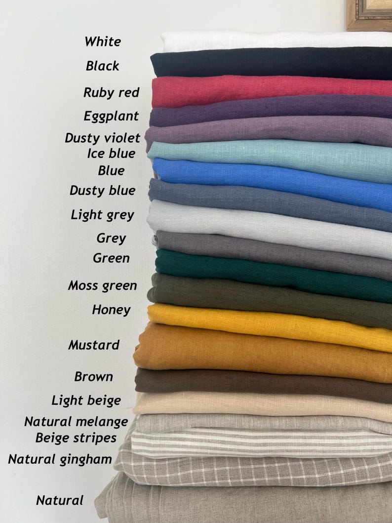 May include: A stack of folded fabric samples in various colors, including white, black, ruby red, and mustard. The image displays the names of the colors: White, Black, Ruby red, Eggplant, Dusty violet, Ice blue, Blue, Dusty blue, Light grey, Grey, Green, Moss green, Honey, Mustard, Brown, Light beige, Natural melange, Beige stripes, Natural gingham, and Natural.