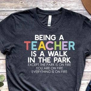 May include: A dark grey t-shirt with the text "Being a Teacher is a walk in the park except the park is on fire you are on fire everything is on fire" in colorful letters.