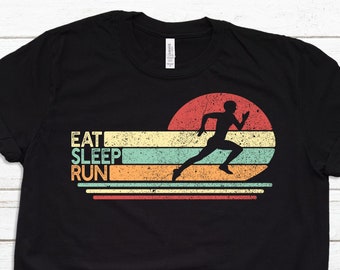 May include: Black t-shirt with the words "EAT SLEEP RUN" and a running figure silhouetted against a retro sunset design. The shirt is paired with blue jeans and white sneakers, suggesting athletic wear.
