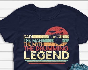 Puede incluir: Una camiseta azul marino con un gráfico de estilo vintage de una batería y el texto "Dad The Man The Myth The Drumming Legend".