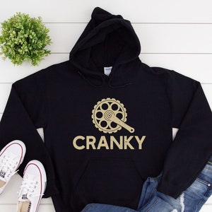 May include: Black hoodie with a gold bicycle chain graphic and the word "CRANKY" printed on the front.