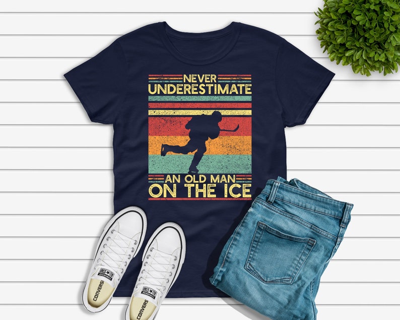 May include: A navy blue t-shirt with a vintage-style graphic of a hockey player skating. The graphic includes the text "Never underestimate an old man on the ice".