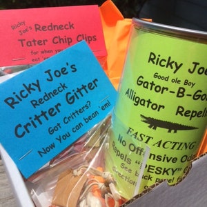 May include: A box filled with three different products: a red and white package labeled "Ricky Joe's Redneck Tater Chip Clips", a blue and white package labeled "Ricky Joe's Redneck Critter Gitter", and a green can labeled "Ricky Joe Good ole Boy Gator-B-Gone Alligator Repellent".