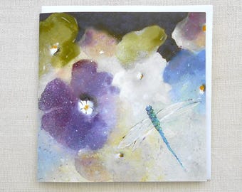 May include: A square greeting card with a watercolour painting of flowers in purple, blue, and green hues. A blue dragonfly is painted in the foreground. The card has a white border and is blank inside.