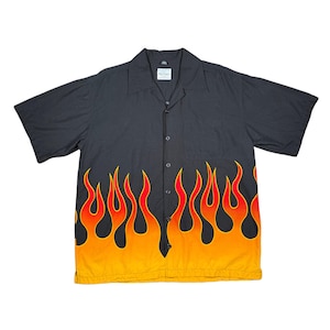 May include: Black button-down short-sleeve shirt with a flame design. The flames are red, orange, and yellow, creating a vibrant contrast against the black fabric. The shirt has a classic collar and a relaxed fit.