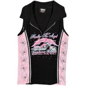 May include: Black sleeveless top with a zip-up front and a collared neckline. The top features pink side panels with floral designs and a graphic on the front that says "Hardly An Angel" with a motorcycle and angel wings. The text "Daytona Beach" is also visible.