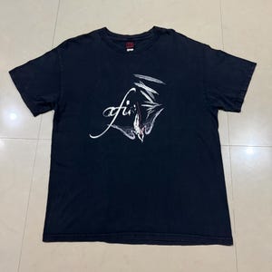 May include: Black t-shirt featuring the band name "afi" in white script with a stylized graphic. The shirt has short sleeves and a crew neck. The fabric appears worn, giving it a vintage look.