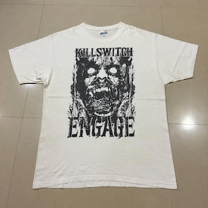 Puede incluir: Camiseta blanca con un gráfico en blanco y negro de una cara de zombi y el texto "KILLSWITCH ENGAGE". La camiseta está hecha de un material suave y cómodo.