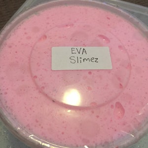 Puede incluir: Slime rosa en un recipiente de plástico transparente con una etiqueta blanca que dice "EVA Slimez".