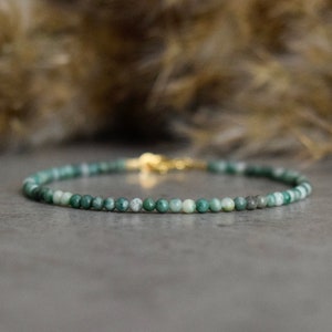 May include: A delicate green and white beaded bracelet with a gold clasp.