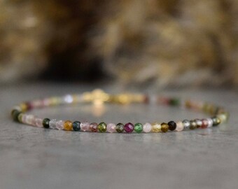 May include: A dainty bracelet featuring small, multicoloured gemstone beads. The beads are a blend of pink, green, brown, and clear.