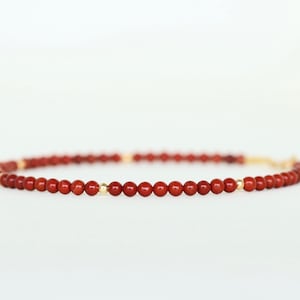 May include: A red gemstone bracelet with gold beads.