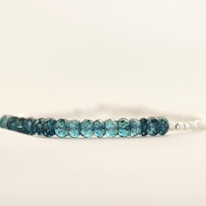 May include: A delicate bracelet featuring a row of blue gemstone beads on a silver chain.