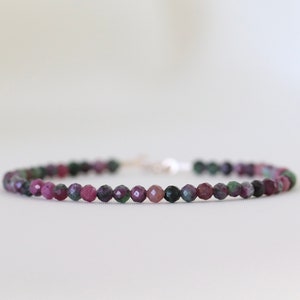 May include: A delicate bracelet made with small, faceted beads in shades of pink, green, and black. The beads are strung on a silver chain.