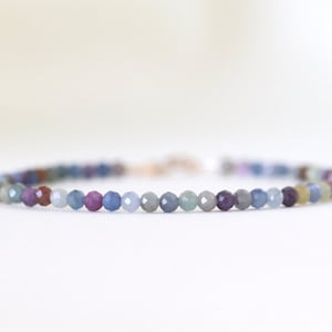 May include: A delicate bracelet made with small, faceted beads in shades of blue, purple, and green. The beads are strung on a silver chain.