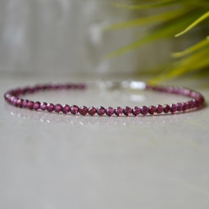 K&ouml;nnte beinhalten: Ein zartes Armband aus kleinen, facettierten, dunkelrosa Edelsteinen. Das Armband ist auf einer silbernen Kette aufgef&auml;delt.