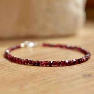 May include: A delicate bracelet made with small, dark red garnet beads. The bracelet is strung on a silver chain and has a simple clasp.