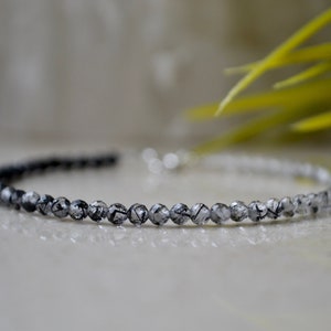 May include: A delicate bracelet made of small, round, clear quartz beads with black inclusions. The beads are strung on a silver chain.