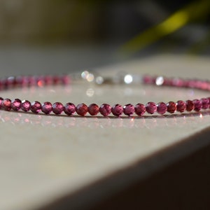 K&ouml;nnte beinhalten: Ein zartes Armband aus rosafarbenen Edelsteinen mit einem silbernen Verschluss. Das Armband besteht aus kleinen, facettierten Perlen.